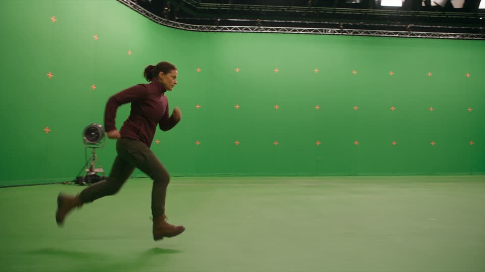Darstellerin läuft vor einer Greenscreen-Wand mit Tracking-Markern im Studio